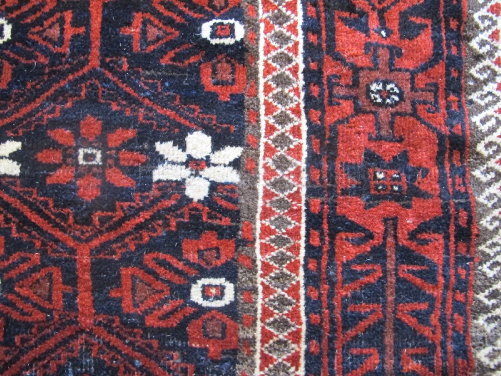 An antique Balouchi handwoven wool runner rug displaying repeating geometric star motifs in deep red, navy, and ivory tones on a dark background. View VII