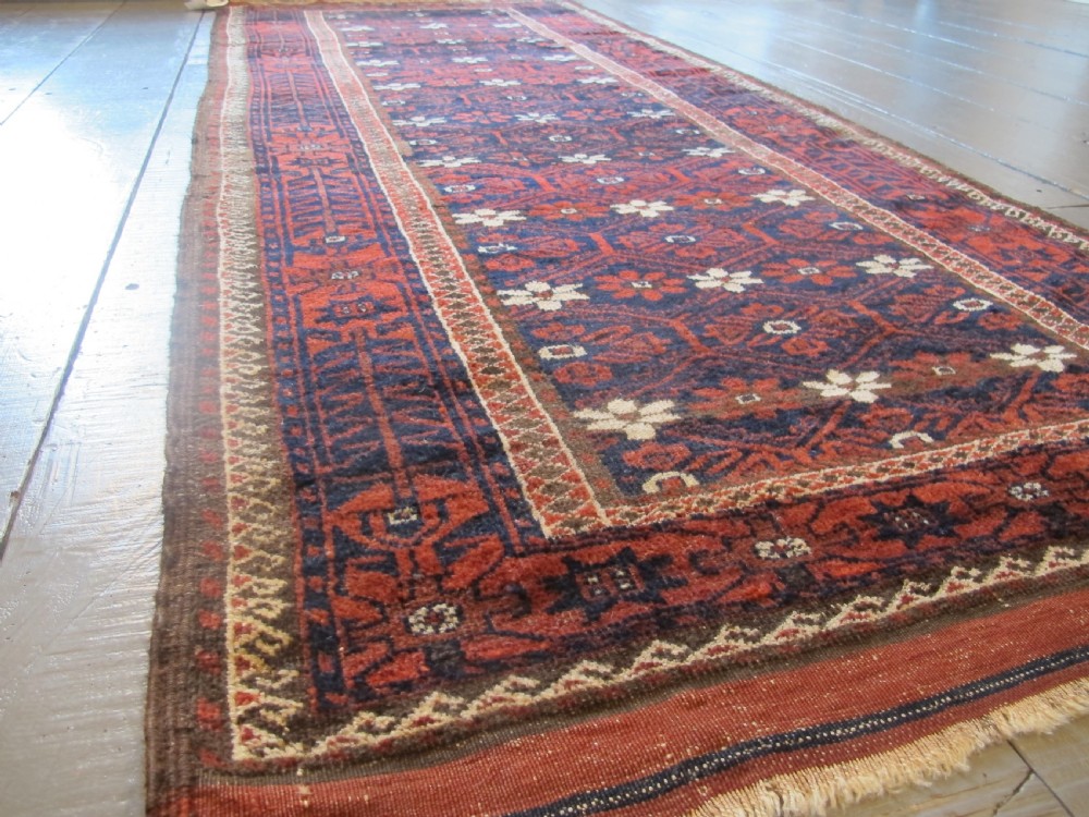An antique Balouchi handwoven wool runner rug displaying repeating geometric star motifs in deep red, navy, and ivory tones on a dark background. View IX