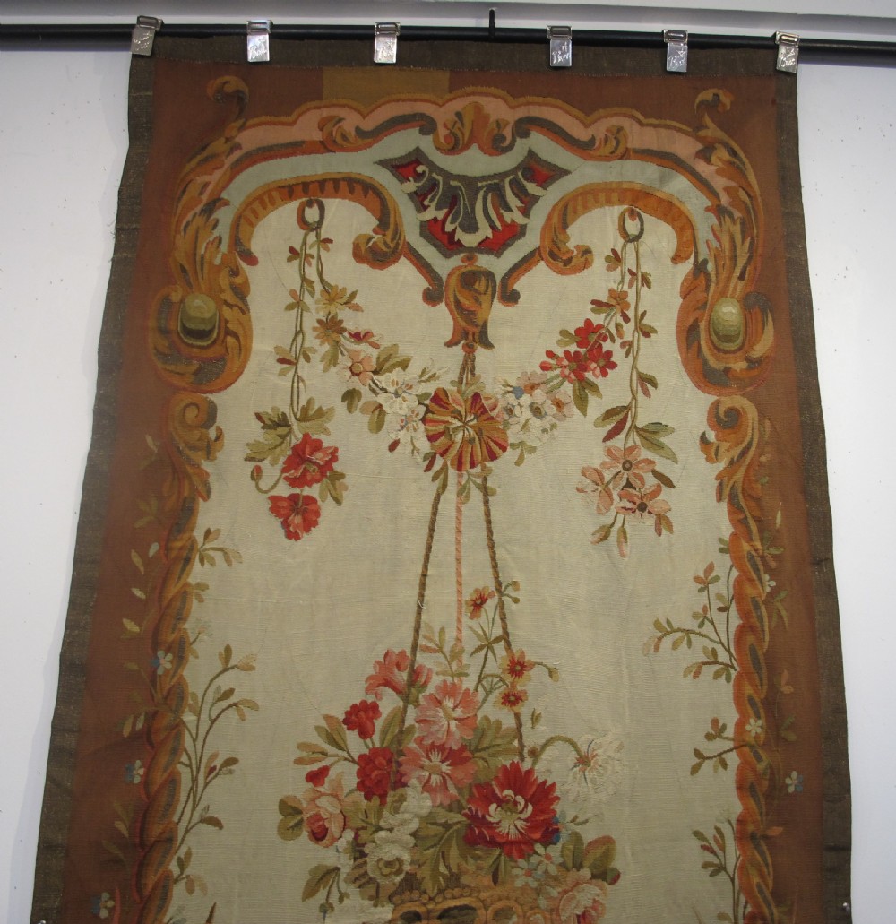 A tall, narrow 19th-century French Aubusson woven tapestry featuring a hanging floral basket, urn motifs, and rocaille border designs on a beige ground. View II