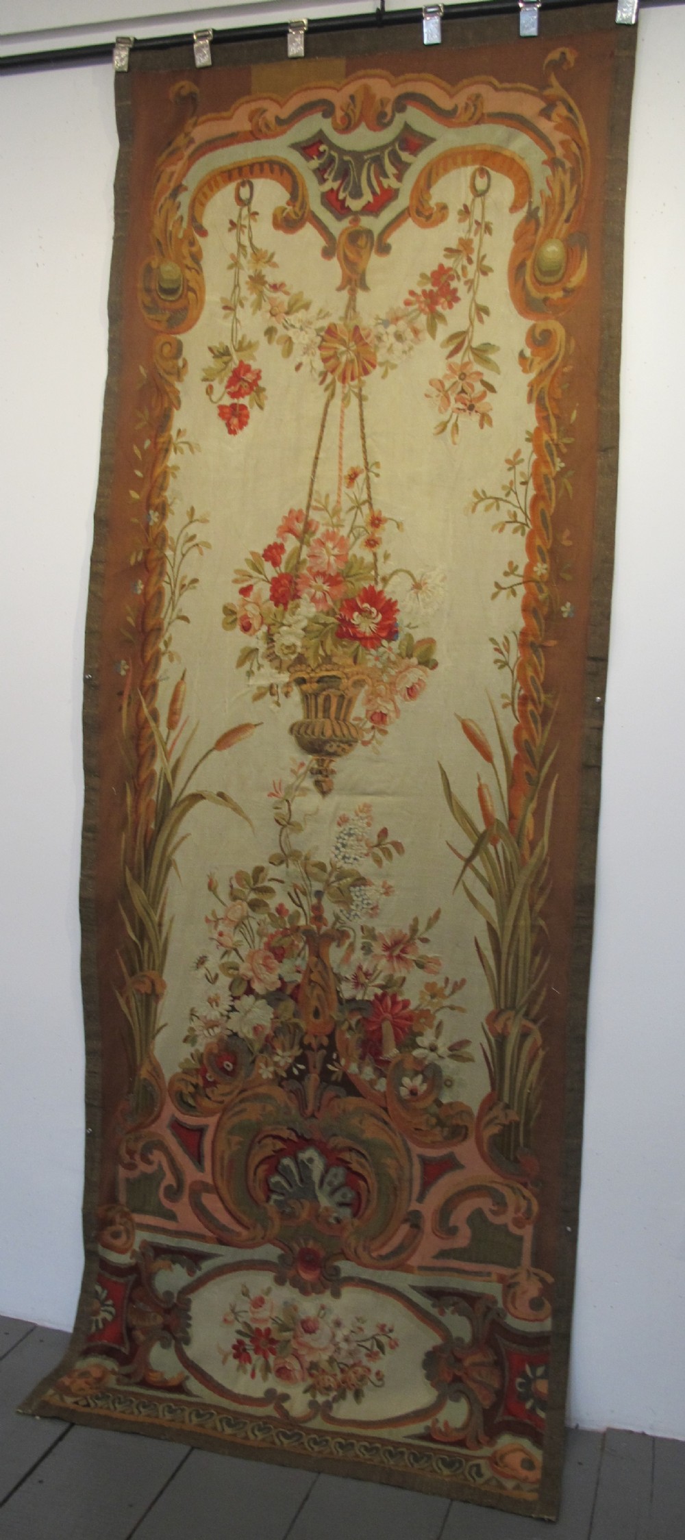 A tall, narrow 19th-century French Aubusson woven tapestry featuring a hanging floral basket, urn motifs, and rocaille border designs on a beige ground. View X