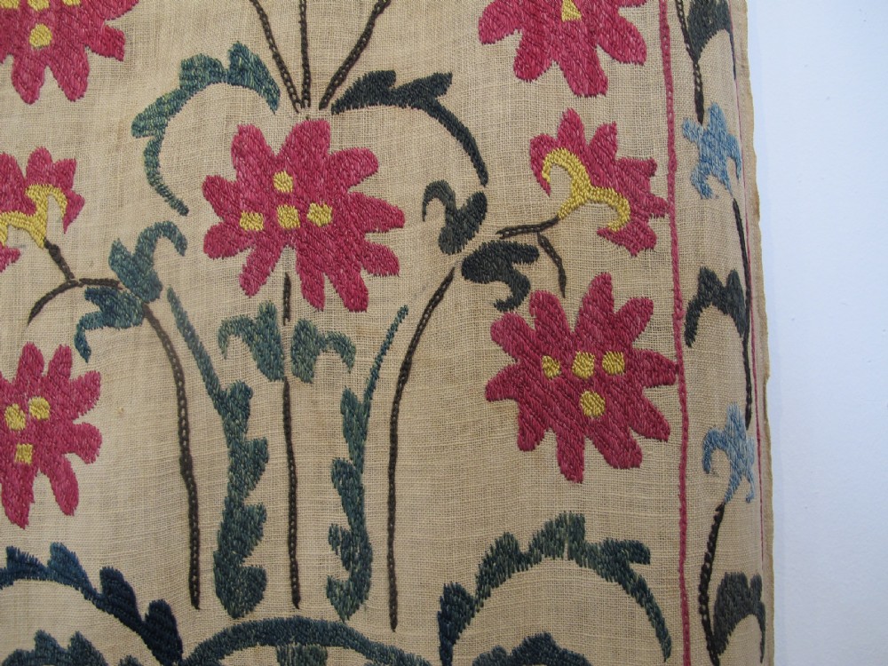 A large rectangular Central Asian suzani textile featuring repeating vertical columns of red embroidered floral motifs on a natural beige cotton substrate. View V