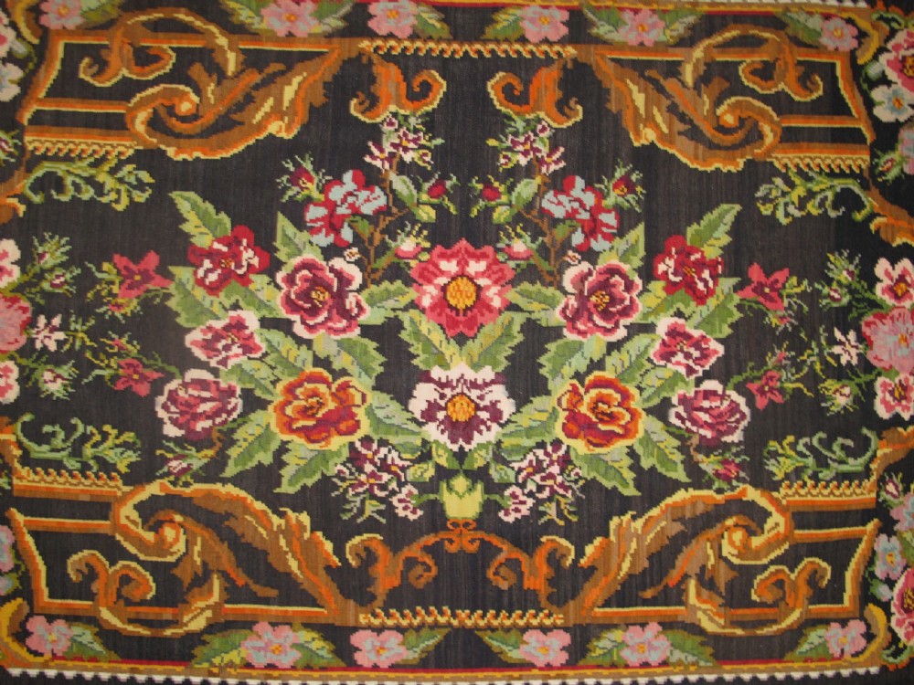 A large rectangular handwoven flatweave rug featuring vibrant floral bouquets and scrollwork borders on a dark black field. View II