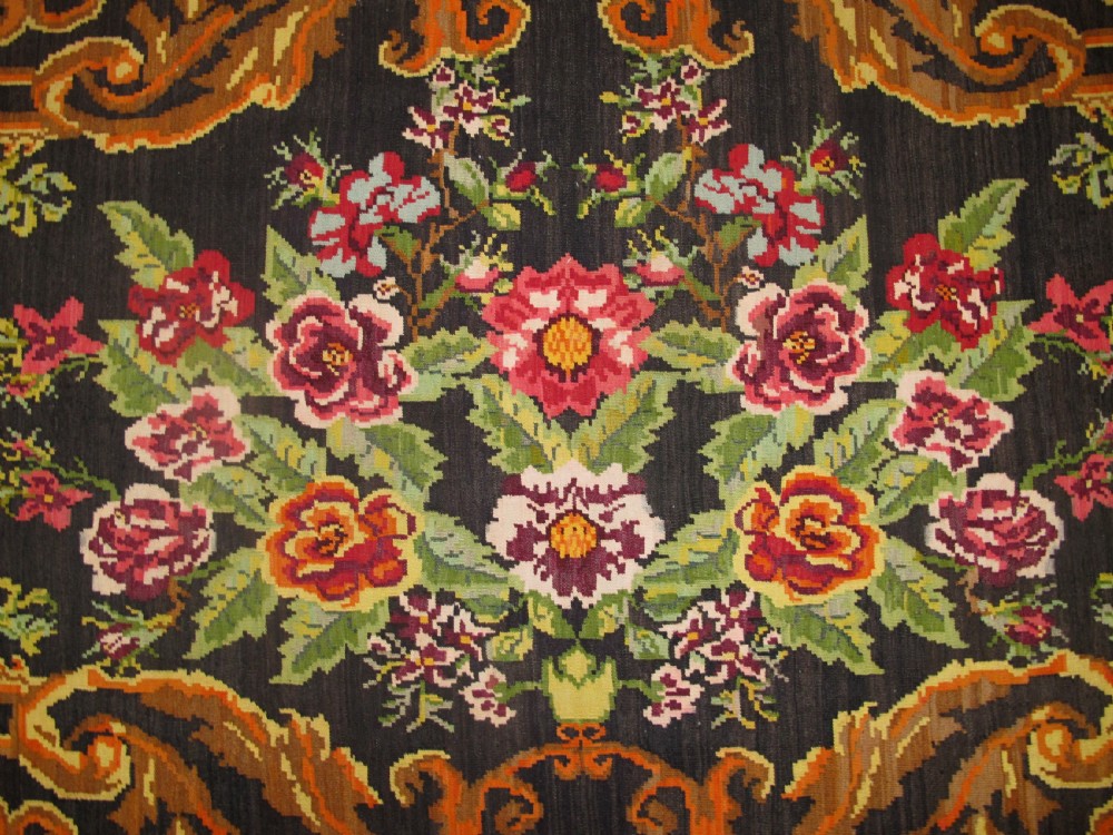 A large rectangular handwoven flatweave rug featuring vibrant floral bouquets and scrollwork borders on a dark black field. View III