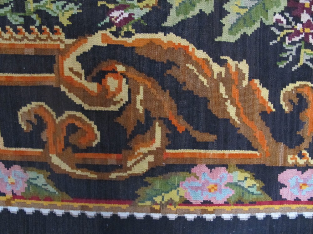 A large rectangular handwoven flatweave rug featuring vibrant floral bouquets and scrollwork borders on a dark black field. View IV