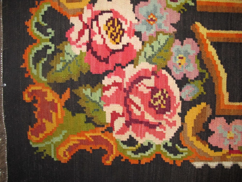 A large rectangular handwoven flatweave rug featuring vibrant floral bouquets and scrollwork borders on a dark black field. View V