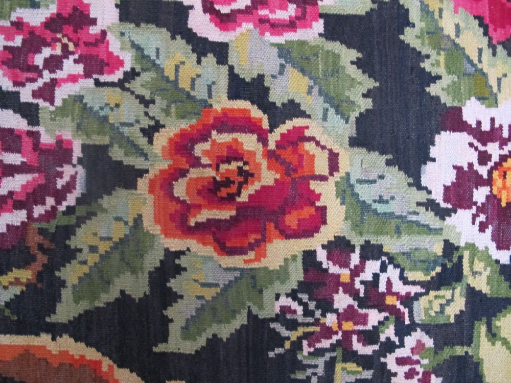 A large rectangular handwoven flatweave rug featuring vibrant floral bouquets and scrollwork borders on a dark black field. View VI