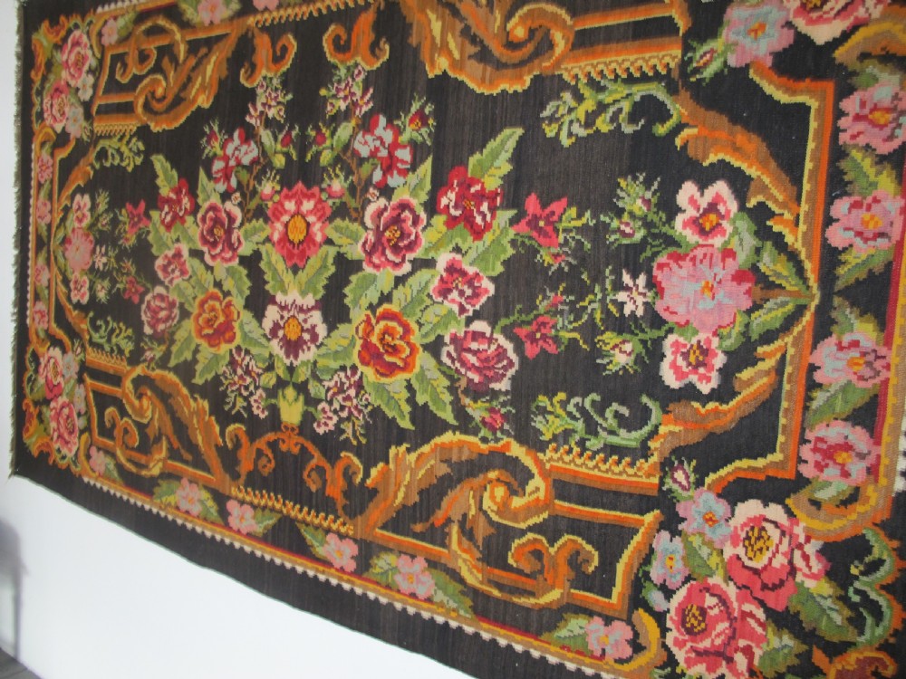 A large rectangular handwoven flatweave rug featuring vibrant floral bouquets and scrollwork borders on a dark black field. View VII