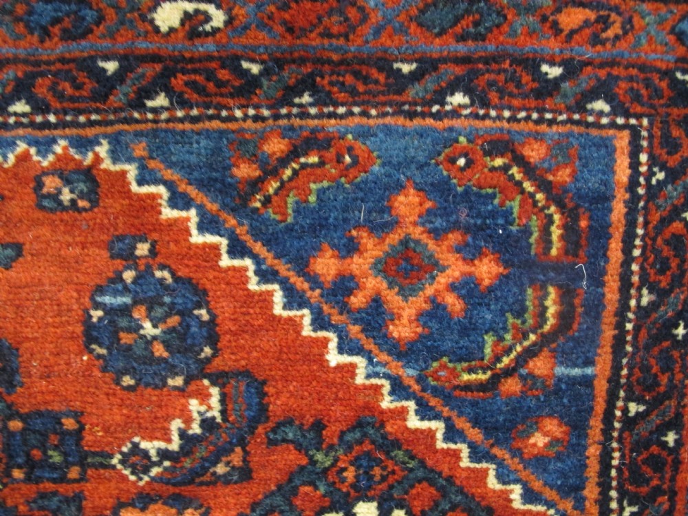 An antique West Persian Melayir wool rug featuring a deep red central field filled with repeating geometric floral motifs within a dark navy multi-tiered border. View II