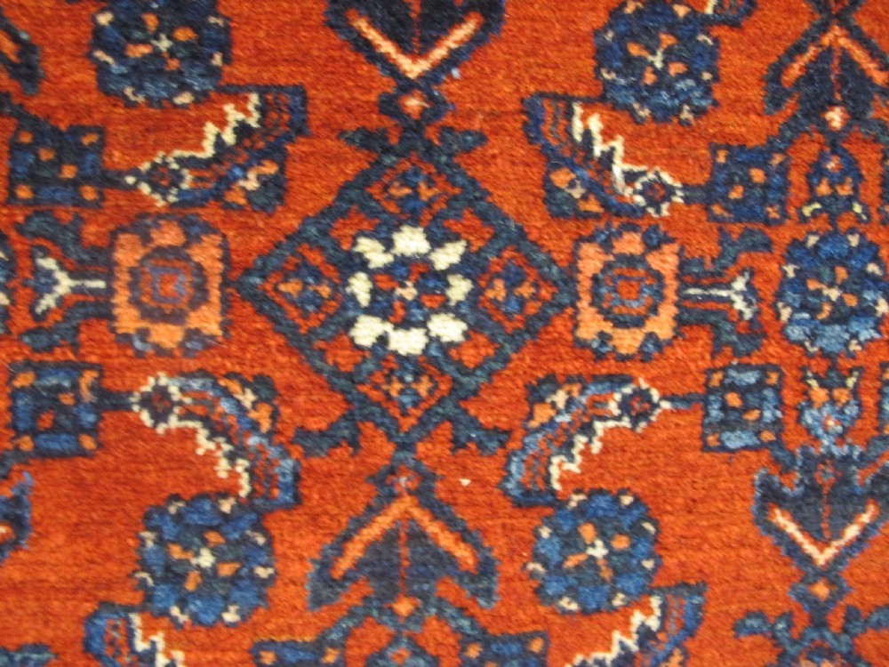 An antique West Persian Melayir wool rug featuring a deep red central field filled with repeating geometric floral motifs within a dark navy multi-tiered border. View III