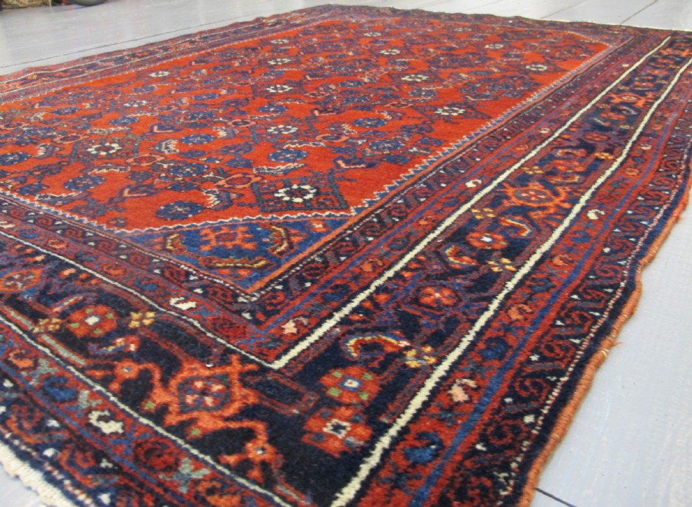 An antique West Persian Melayir wool rug featuring a deep red central field filled with repeating geometric floral motifs within a dark navy multi-tiered border. View VII
