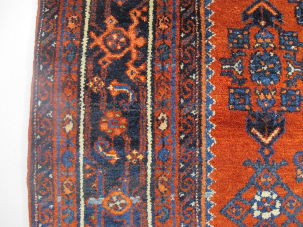 An antique West Persian Melayir wool rug featuring a deep red central field filled with repeating geometric floral motifs within a dark navy multi-tiered border. View VIII