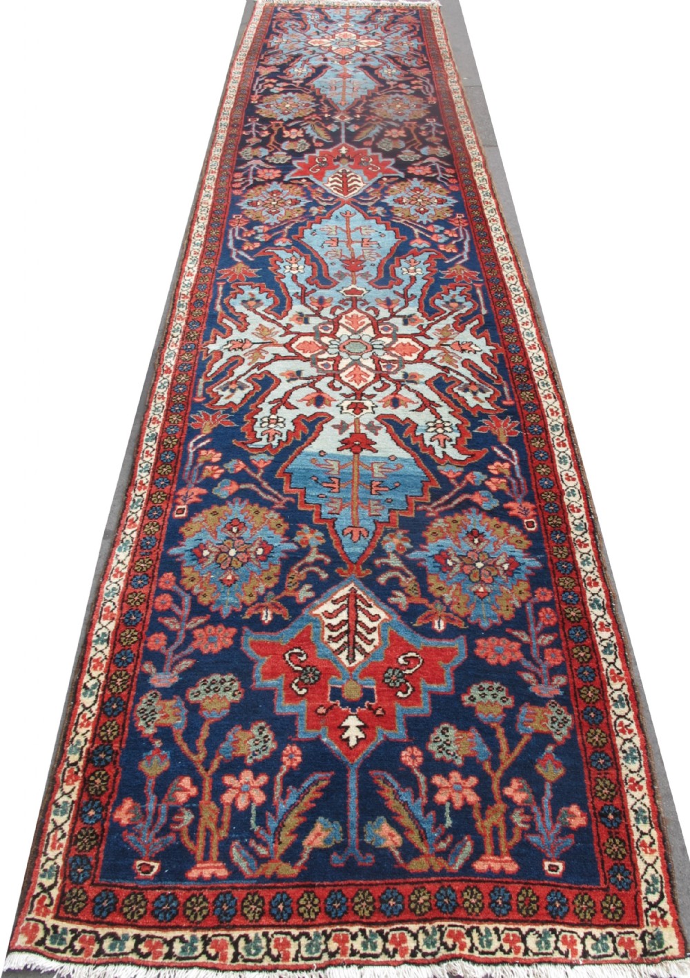 A long, narrow hand-knotted Persian wool runner featuring intricate geometric floral medallions in shades of navy blue, terracotta red, and sky blue along a dark central field.
