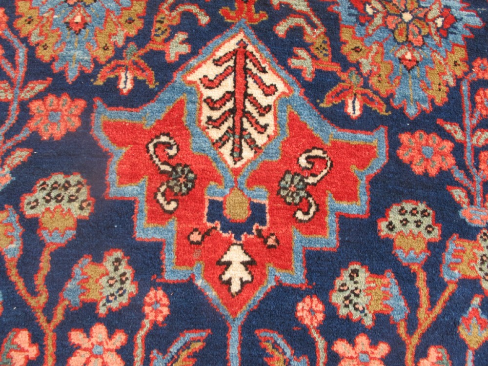 A long, narrow hand-knotted Persian wool runner featuring intricate geometric floral medallions in shades of navy blue, terracotta red, and sky blue along a dark central field. View III