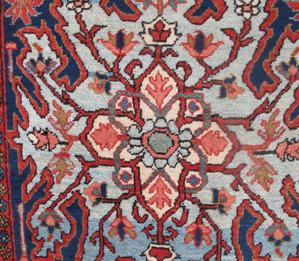 A long, narrow hand-knotted Persian wool runner featuring intricate geometric floral medallions in shades of navy blue, terracotta red, and sky blue along a dark central field. View V