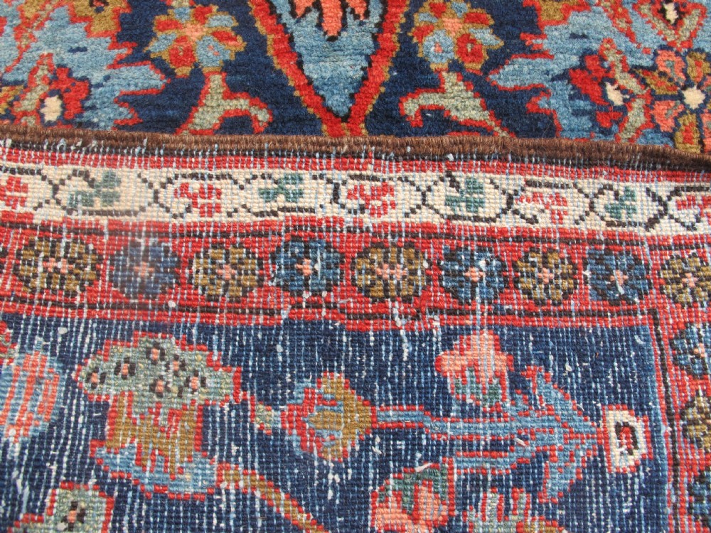A long, narrow hand-knotted Persian wool runner featuring intricate geometric floral medallions in shades of navy blue, terracotta red, and sky blue along a dark central field. View VI