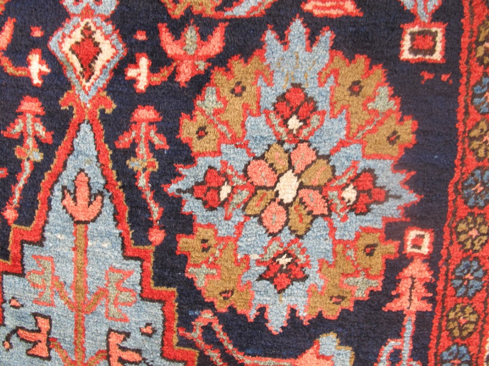 A long, narrow hand-knotted Persian wool runner featuring intricate geometric floral medallions in shades of navy blue, terracotta red, and sky blue along a dark central field. View X