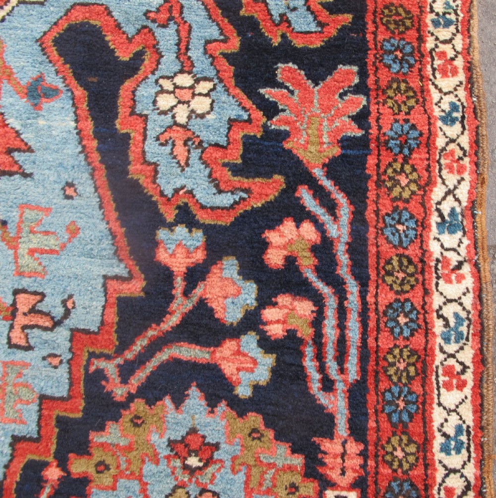 A long, narrow hand-knotted Persian wool runner featuring intricate geometric floral medallions in shades of navy blue, terracotta red, and sky blue along a dark central field. View XII