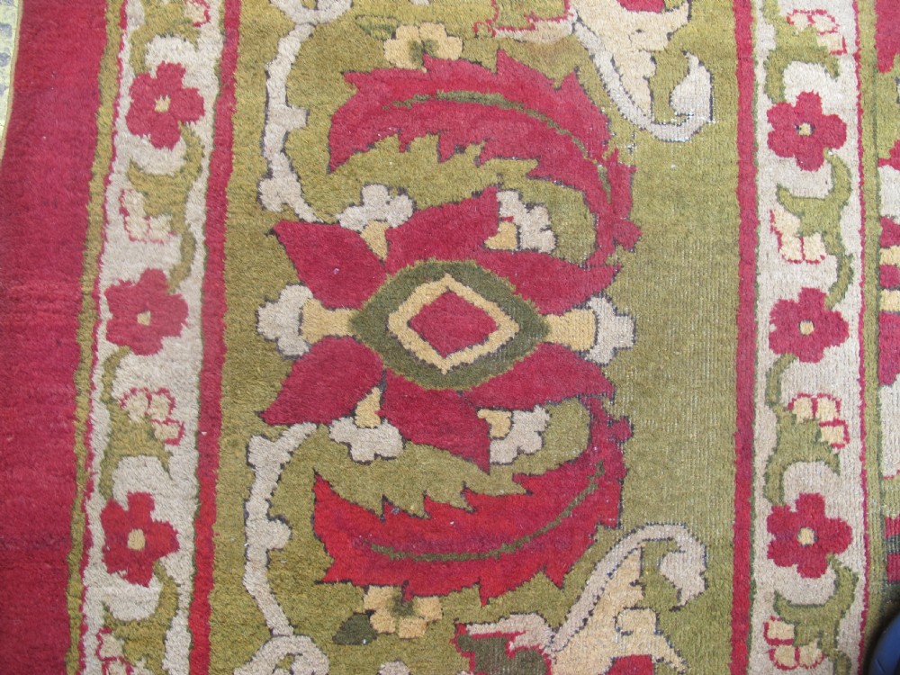 A large hand-knotted wool Amritsar carpet featuring a crimson red field decorated with olive green, cream, and pink floral vine arabesques. View X