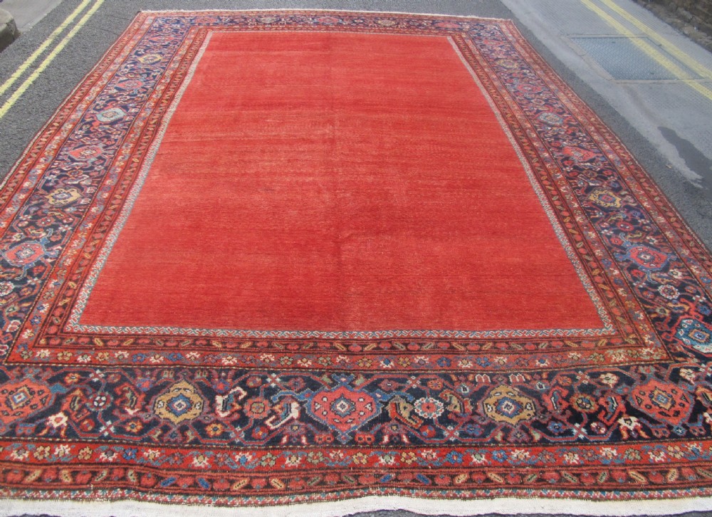 A large late 19th-century Persian Fereghan carpet featuring an unadorned terracotta red open field within a dark navy and polychrome floral border.