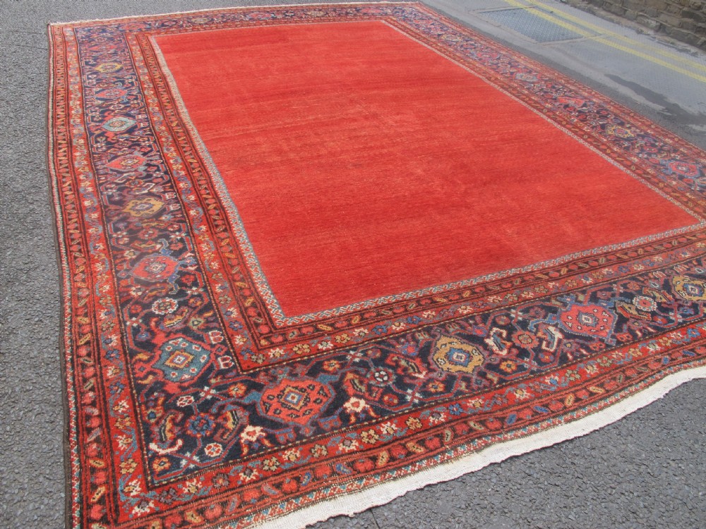 A large late 19th-century Persian Fereghan carpet featuring an unadorned terracotta red open field within a dark navy and polychrome floral border. View II