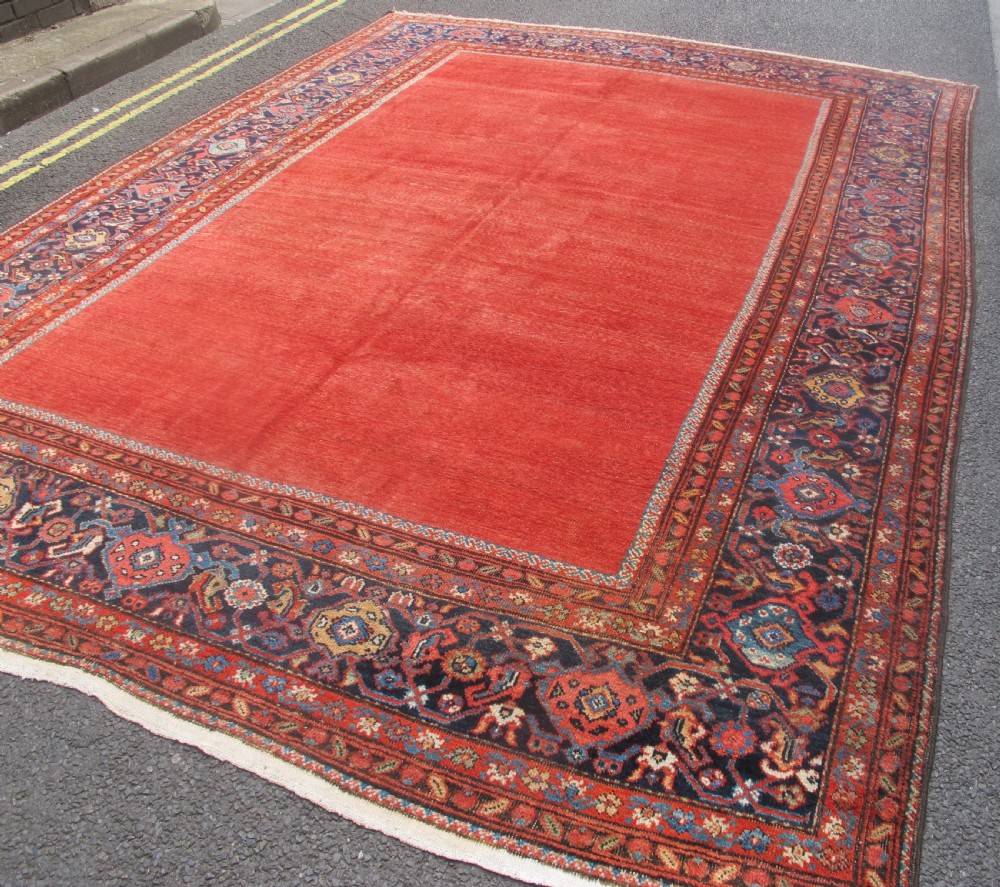 A large late 19th-century Persian Fereghan carpet featuring an unadorned terracotta red open field within a dark navy and polychrome floral border. View III