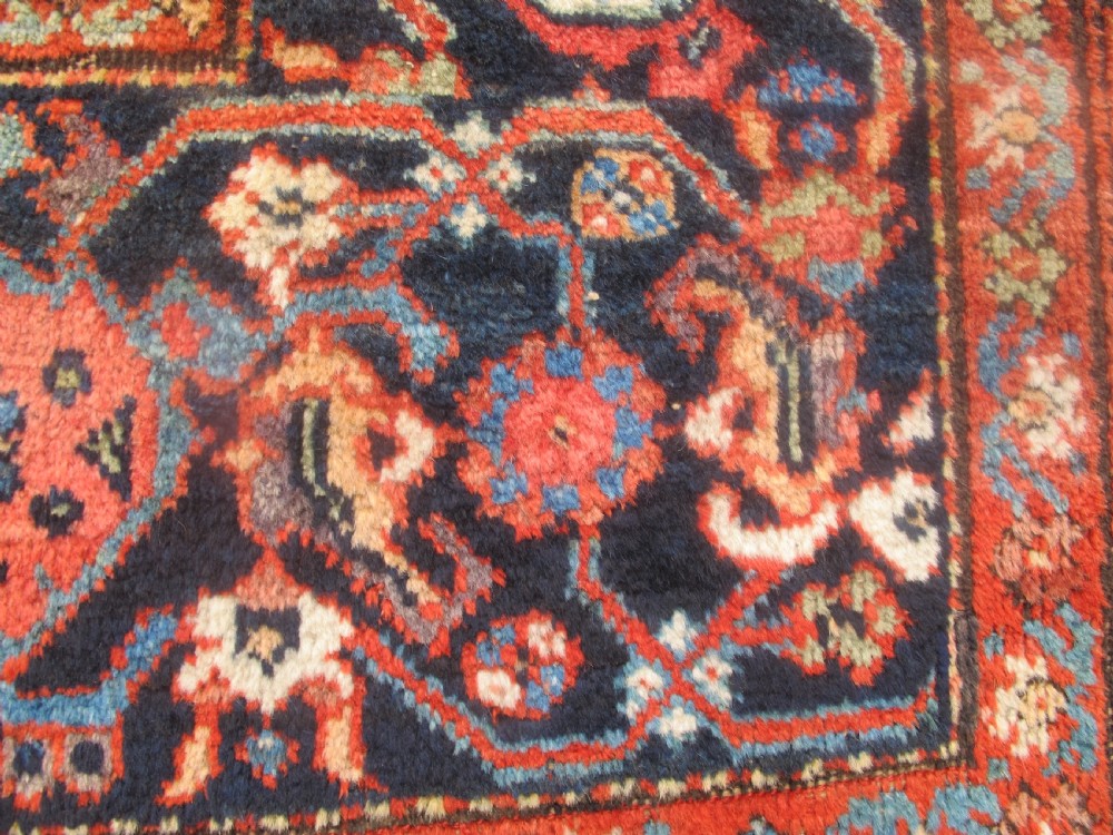 A large late 19th-century Persian Fereghan carpet featuring an unadorned terracotta red open field within a dark navy and polychrome floral border. View V