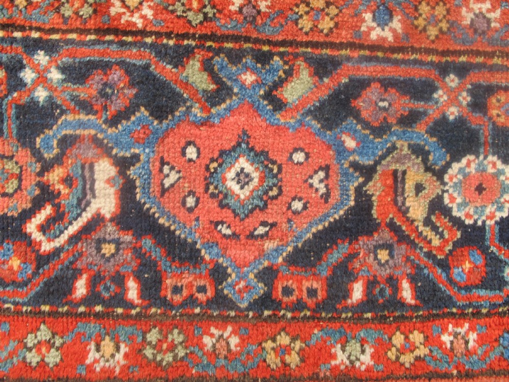 A large late 19th-century Persian Fereghan carpet featuring an unadorned terracotta red open field within a dark navy and polychrome floral border. View VI