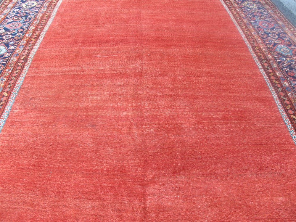 A large late 19th-century Persian Fereghan carpet featuring an unadorned terracotta red open field within a dark navy and polychrome floral border. View VII