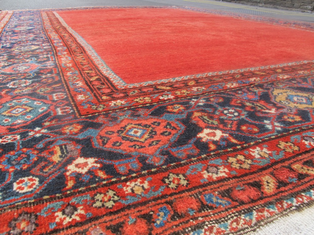 A large late 19th-century Persian Fereghan carpet featuring an unadorned terracotta red open field within a dark navy and polychrome floral border. View VIII