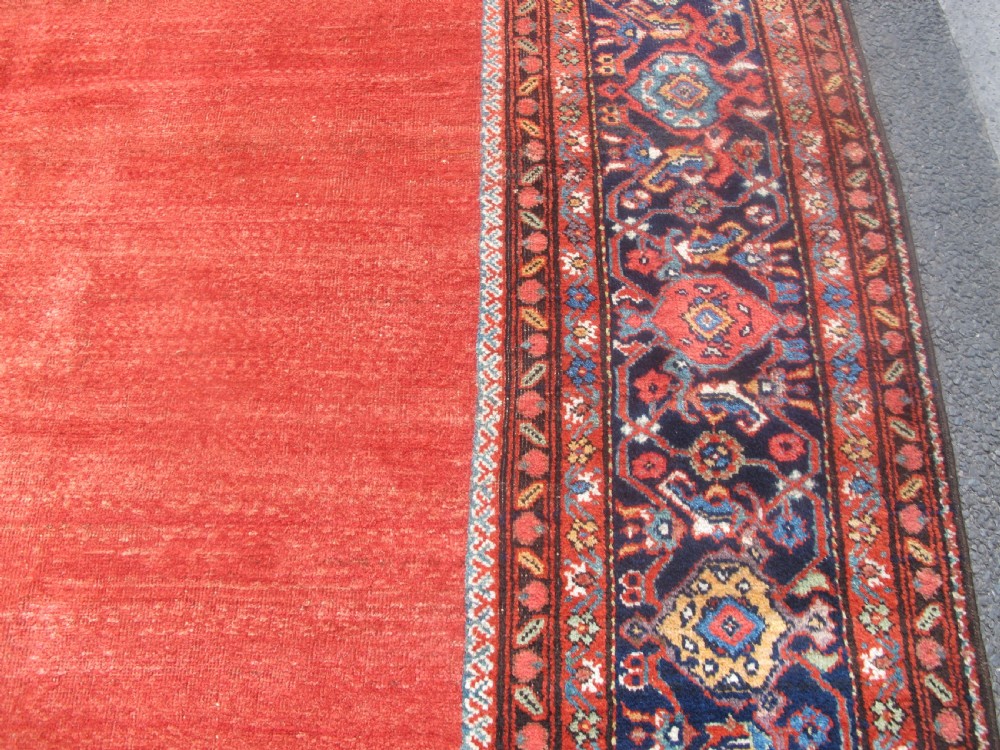 A large late 19th-century Persian Fereghan carpet featuring an unadorned terracotta red open field within a dark navy and polychrome floral border. View IX
