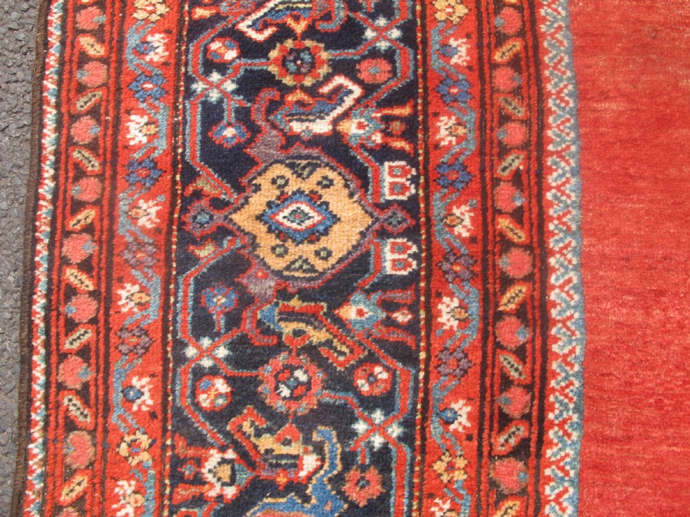 A large late 19th-century Persian Fereghan carpet featuring an unadorned terracotta red open field within a dark navy and polychrome floral border. View X
