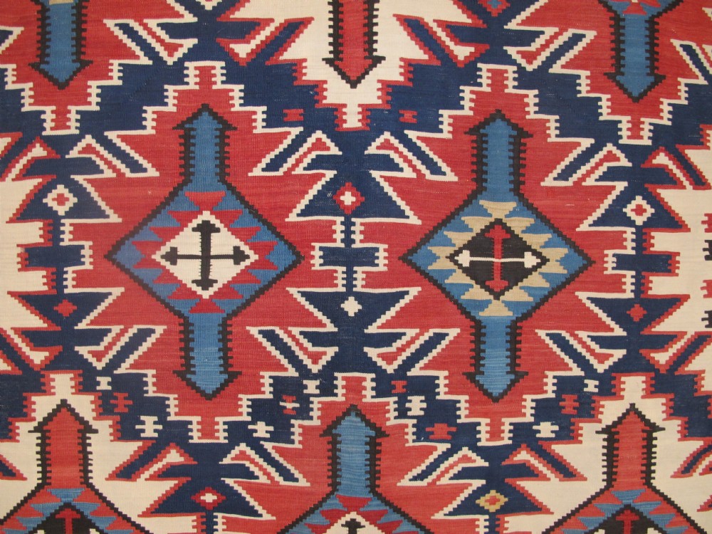 An antique Caucasian kilim flatweave wool rug displaying bold repeating diamond and cross motifs in terracotta red, navy blue, and cream. View II