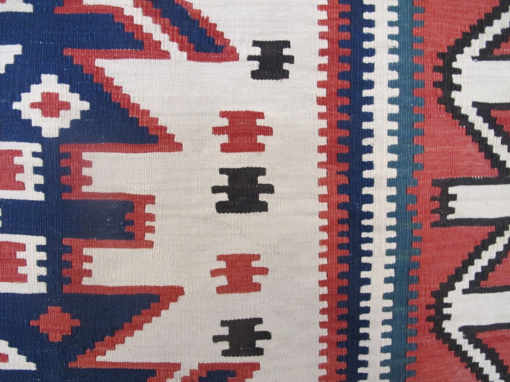 An antique Caucasian kilim flatweave wool rug displaying bold repeating diamond and cross motifs in terracotta red, navy blue, and cream. View V