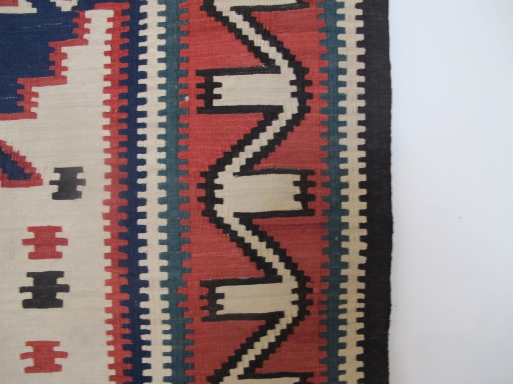 An antique Caucasian kilim flatweave wool rug displaying bold repeating diamond and cross motifs in terracotta red, navy blue, and cream. View VI