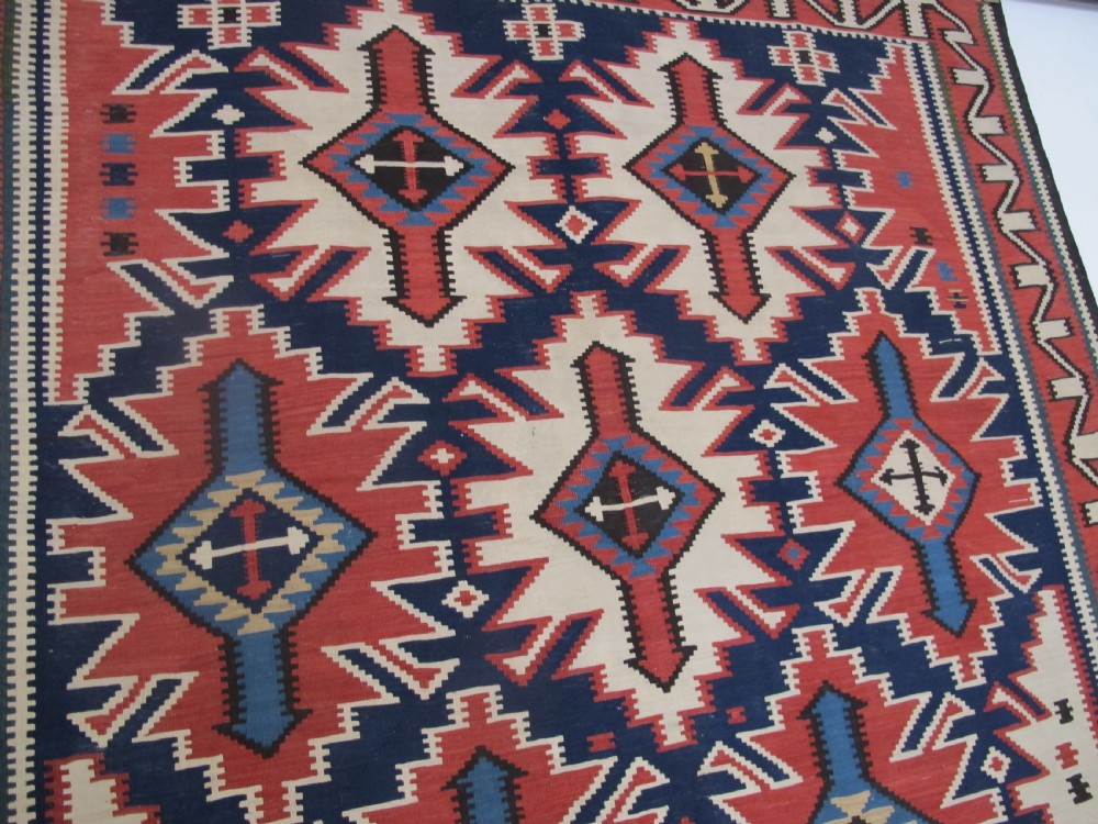 An antique Caucasian kilim flatweave wool rug displaying bold repeating diamond and cross motifs in terracotta red, navy blue, and cream. View VII