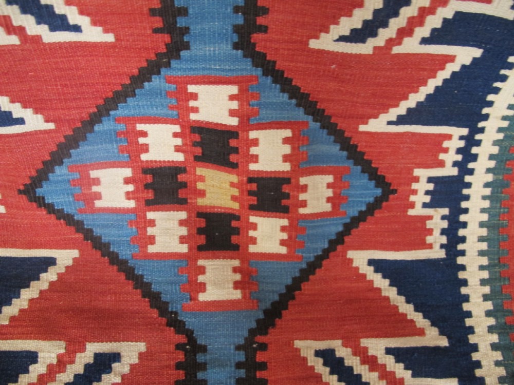 An antique Caucasian kilim flatweave wool rug displaying bold repeating diamond and cross motifs in terracotta red, navy blue, and cream. View VIII
