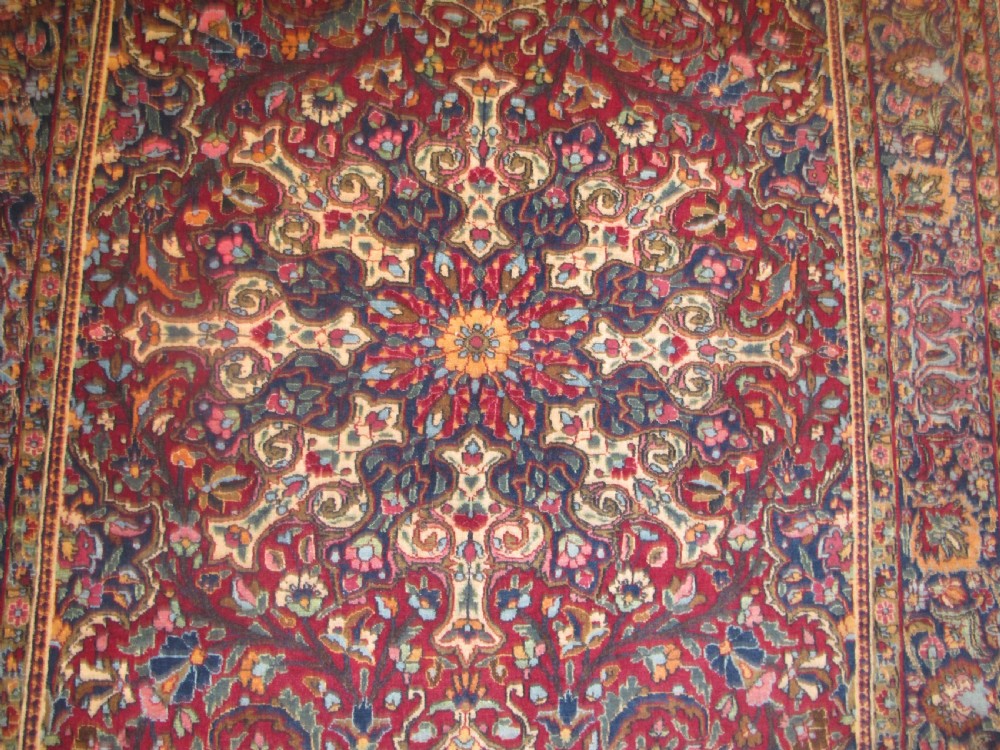 An antique Persian Meshed wool rug featuring an intricate central medallion surrounded by dense floral motifs in crimson red, navy blue, and cream. View VI