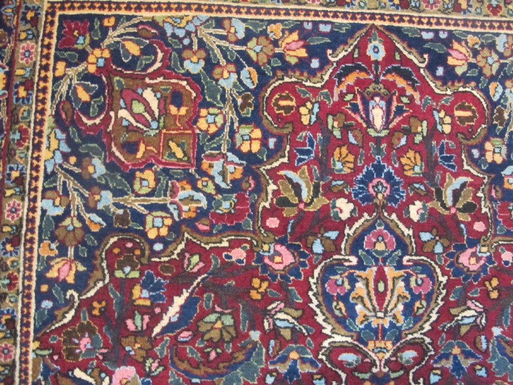 An antique Persian Meshed wool rug featuring an intricate central medallion surrounded by dense floral motifs in crimson red, navy blue, and cream. View VIII