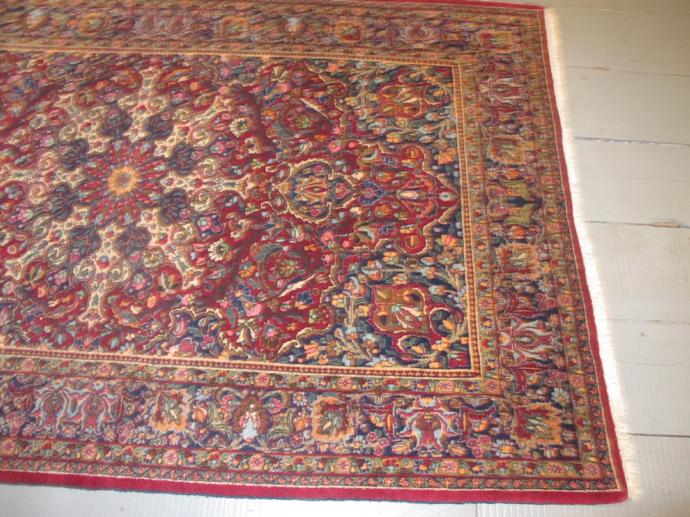 An antique Persian Meshed wool rug featuring an intricate central medallion surrounded by dense floral motifs in crimson red, navy blue, and cream. View X