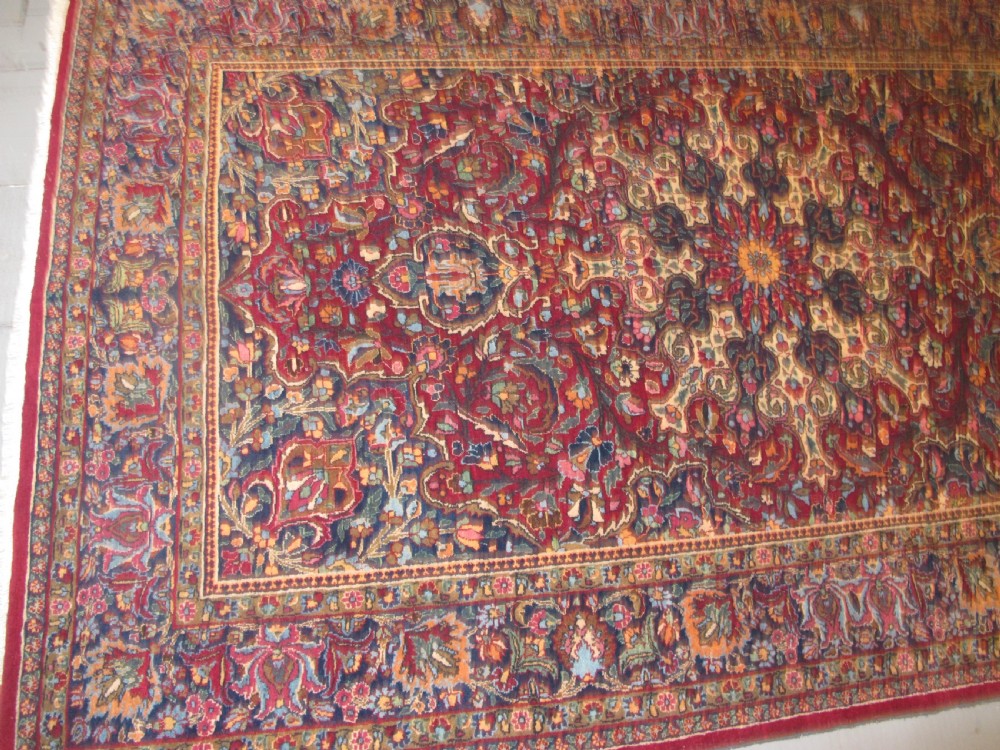 An antique Persian Meshed wool rug featuring an intricate central medallion surrounded by dense floral motifs in crimson red, navy blue, and cream. View XI