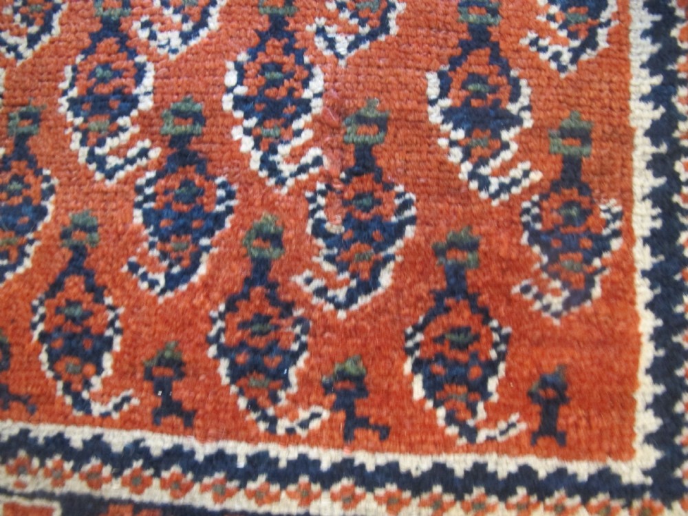 A rectangular hand-knotted wool rug featuring repeating boteh motifs on a red field enclosed by multi-layered cream and navy geometric borders. View VIII