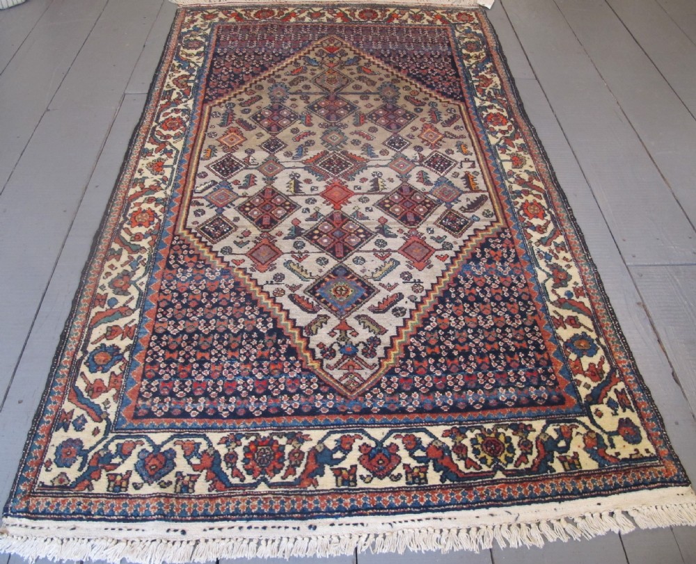 A hand-knotted antique Persian village wool rug featuring a central cream diamond medallion surrounded by geometric motifs and a navy blue field with detailed floral borders.