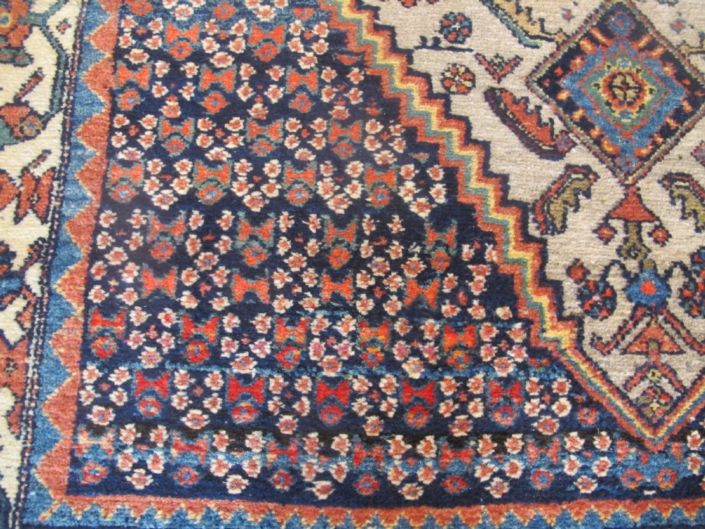 A hand-knotted antique Persian village wool rug featuring a central cream diamond medallion surrounded by geometric motifs and a navy blue field with detailed floral borders. View IV