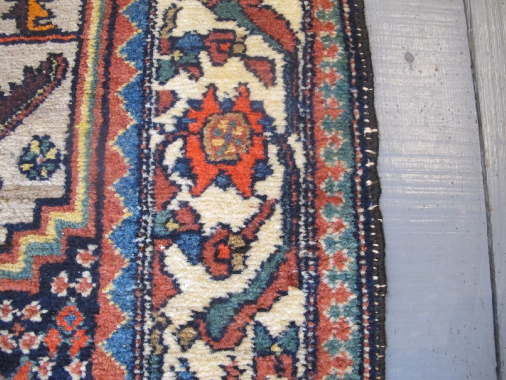 A hand-knotted antique Persian village wool rug featuring a central cream diamond medallion surrounded by geometric motifs and a navy blue field with detailed floral borders. View V