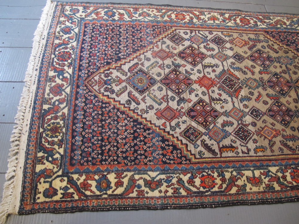 A hand-knotted antique Persian village wool rug featuring a central cream diamond medallion surrounded by geometric motifs and a navy blue field with detailed floral borders. View VII