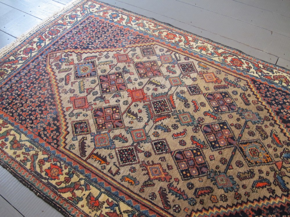 A hand-knotted antique Persian village wool rug featuring a central cream diamond medallion surrounded by geometric motifs and a navy blue field with detailed floral borders. View IX