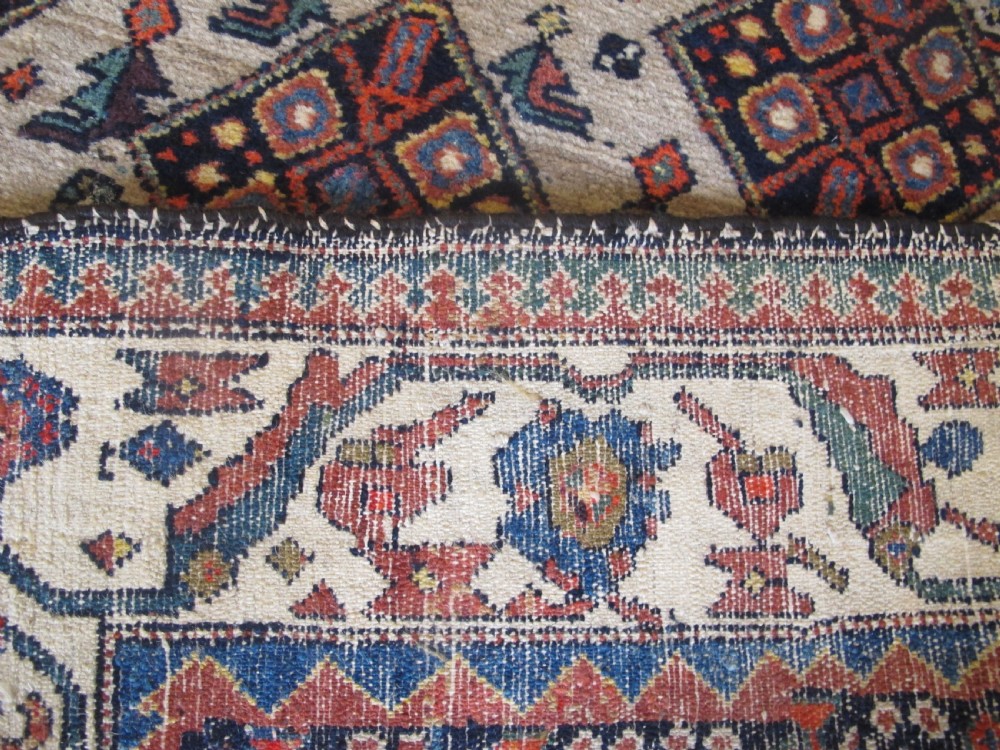 A hand-knotted antique Persian village wool rug featuring a central cream diamond medallion surrounded by geometric motifs and a navy blue field with detailed floral borders. View X