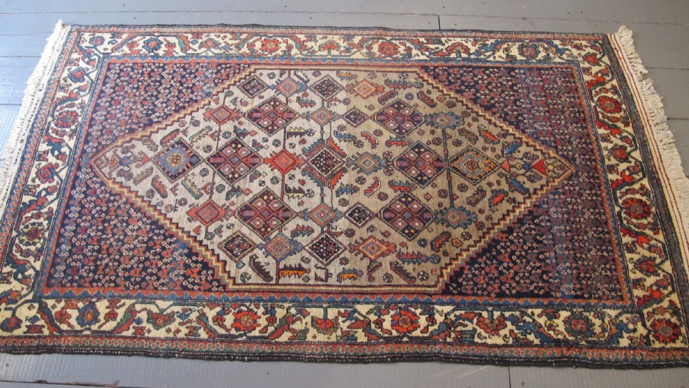 A hand-knotted antique Persian village wool rug featuring a central cream diamond medallion surrounded by geometric motifs and a navy blue field with detailed floral borders. View XI