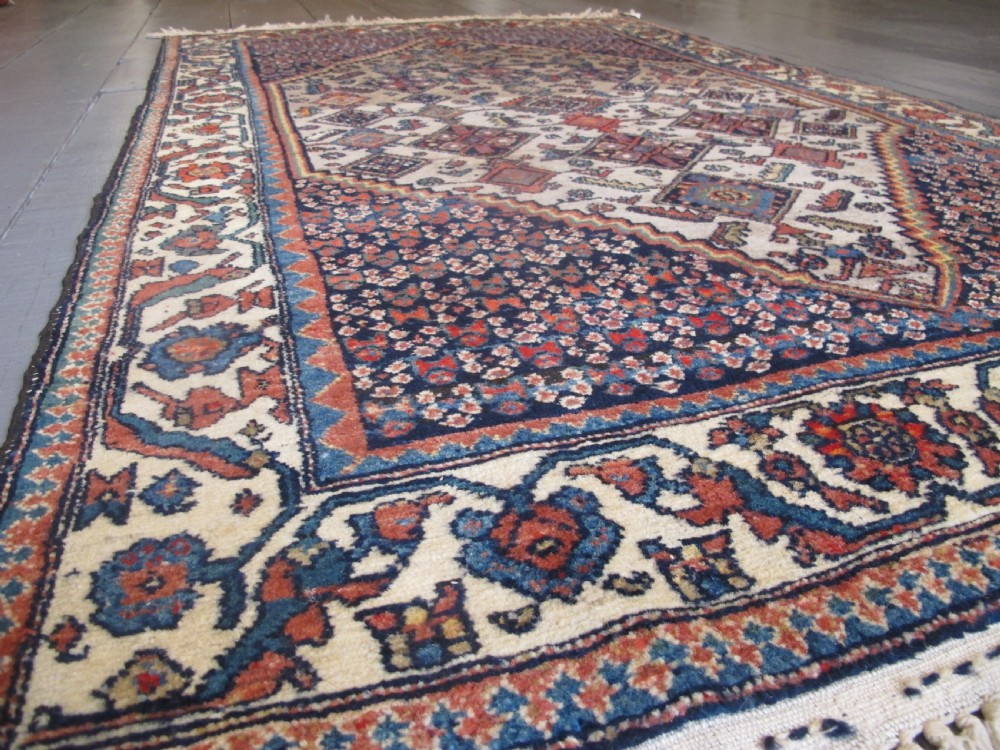 A hand-knotted antique Persian village wool rug featuring a central cream diamond medallion surrounded by geometric motifs and a navy blue field with detailed floral borders. View XII