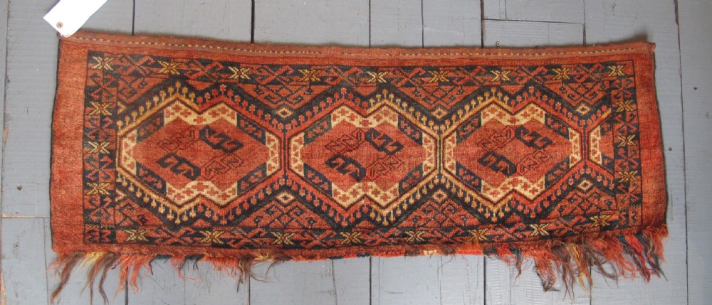 A rectangular handwoven Turkmen wool bagface displaying three repeating geometric diamond medallions in red, navy, and cream with fringed bottom edges.